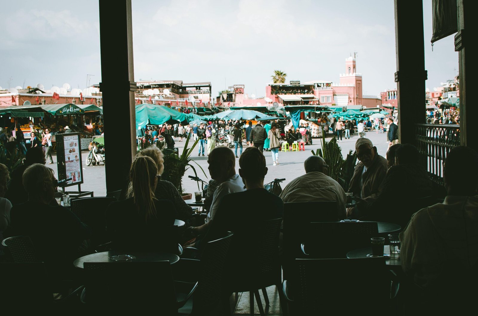 A vibrant Moroccan market filled with people, seen from a shaded cafe.